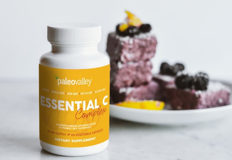 PaleoValley Essential C Complex bottle on a marble surface with a plate of blueberry dessert topped with blueberries and lemon slices in the background.