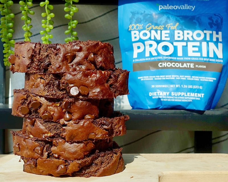 Stack of chocolate banana bread slices made with Paleovalley Chocolate Bone Broth Protein, topped with chocolate chips, with the protein pouch in the background.