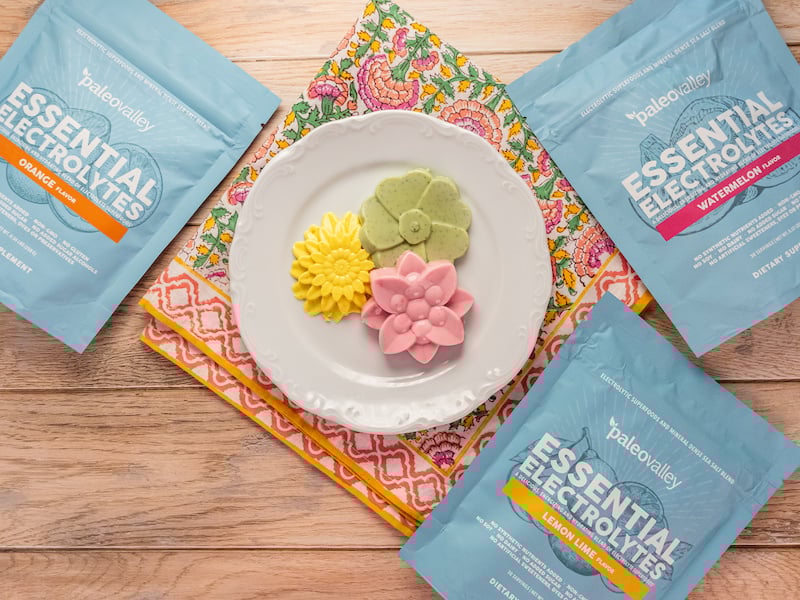 Three creamy, flower-shaped electrolyte gummies on a plate surrounded by Paleovalley Essential Electrolytes packets.