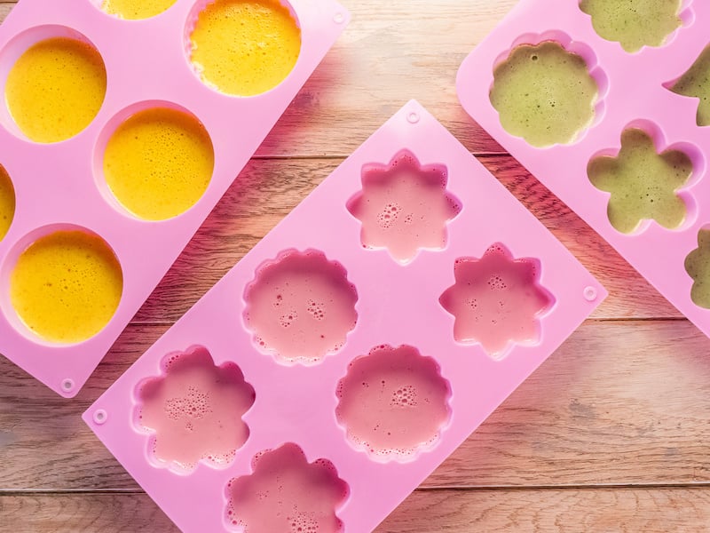 Colorful creamy electrolyte gummy mixtures setting in pink silicone flower molds on a wooden surface.