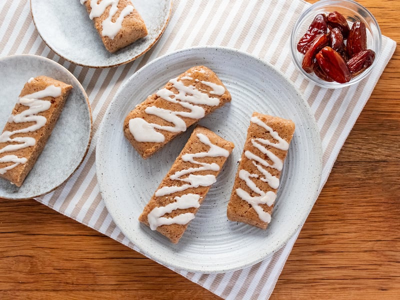 Homemade paleo protein bars drizzled with icing, made using Paleovalley Salted Caramel Bone Broth Protein, served on ceramic plates with a side of medjool dates.