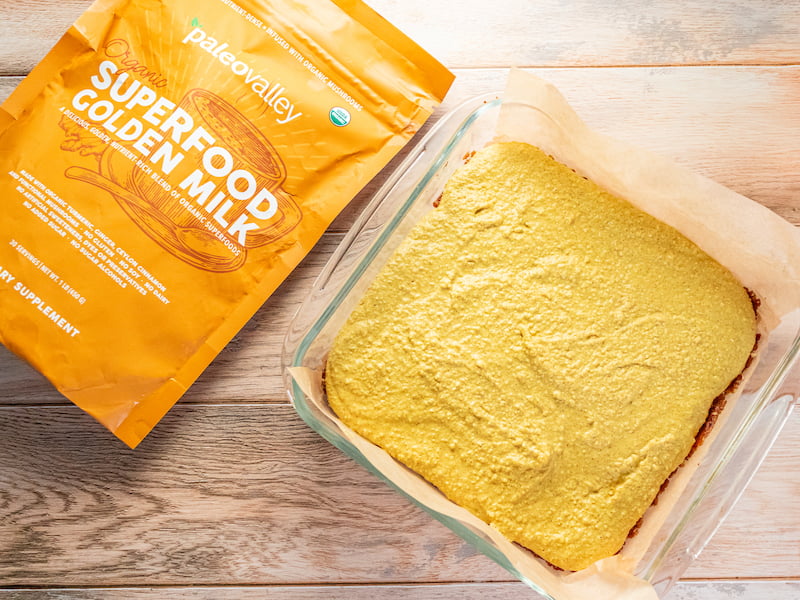 **Alt text:** A glass baking dish filled with golden milk no-bake cheesecake bars next to a bag of Paleovalley Superfood Golden Milk.