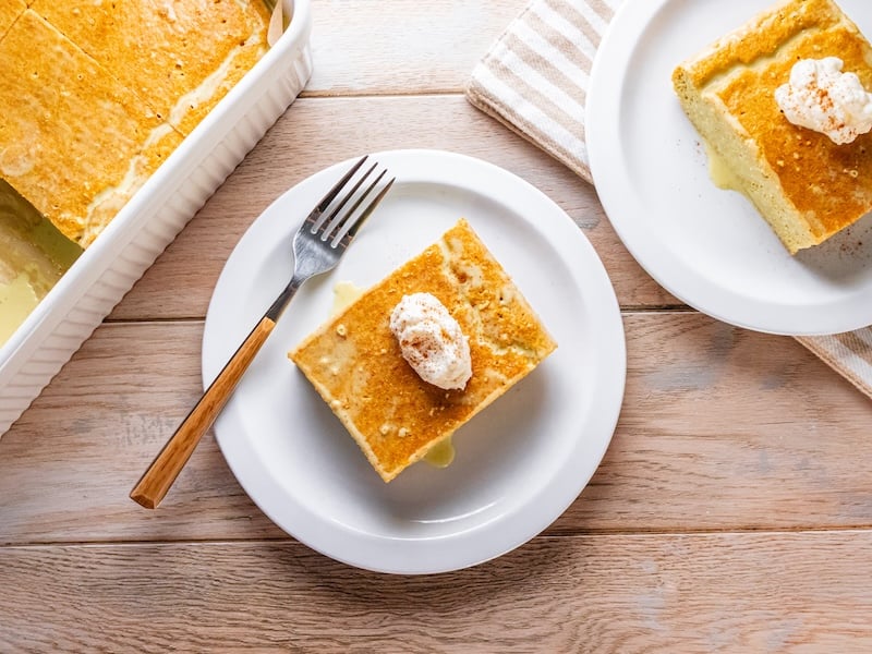 Paleo tres leches cake made with Paleovalley Golden Milk, topped with coconut whipped cream and cinnamon, served on a white plate with a wooden fork.