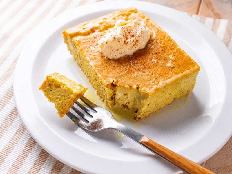 Close-up of a moist slice of golden milk paleo tres leches cake topped with whipped cream and cinnamon, with a bite on a fork.