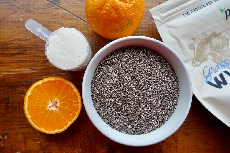 Ingredients for chia pudding: whole chia seeds, a scoop of Paleovalley grass fed whey protein powder, and fresh oranges