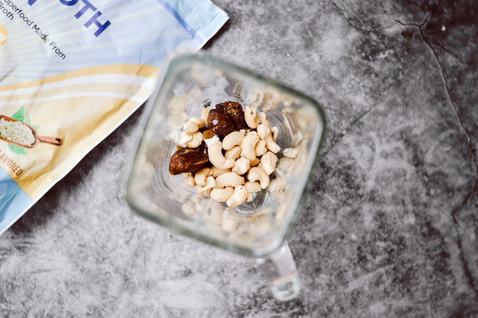Blender filled with cashews and dates next to a bag of Paleovalley bone broth protein.