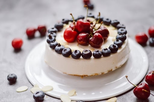 Paleo cherry cheesecake made with Paleovalley Bone Broth Protein, topped with fresh blueberries and cherries on a white plate.