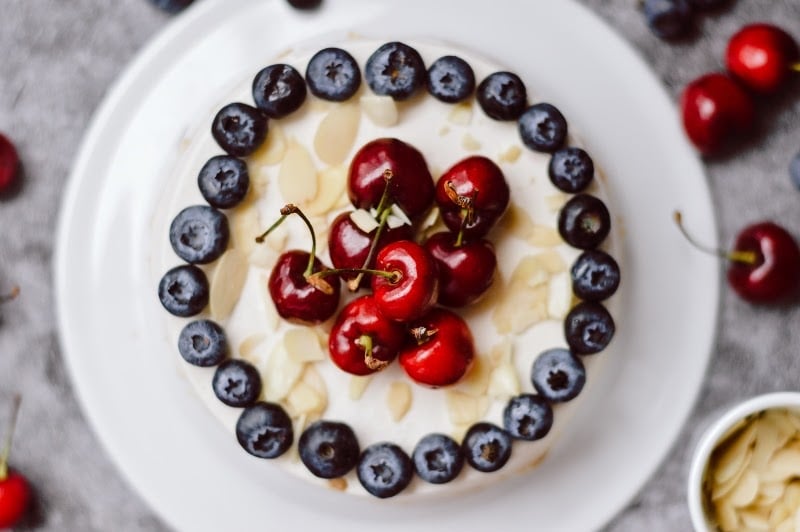 Overhead view of a Paleo cherry cheesecake topped with fresh cherries, blueberries, and sliced almonds, made with Paleovalley Bone Broth Protein.