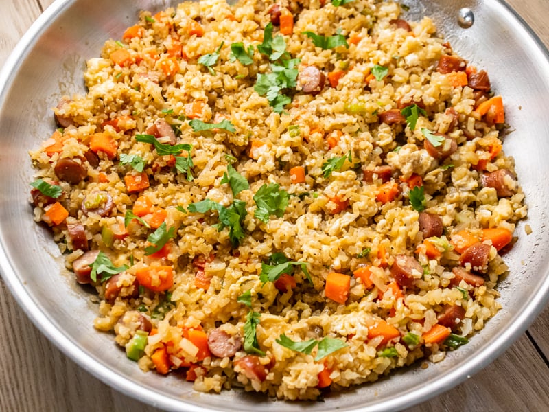 Cauliflower fried rice with chopped vegetables and sliced Paleovalley Teriyaki Chicken Sticks, served on a plate with the product packaging beside it.