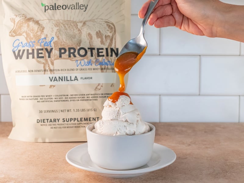 Vanilla protein ice cream drizzled with caramel beside Paleovalley Vanilla Whey Protein.