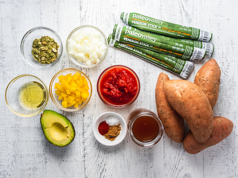 Ingredients for venison chili stuffed sweet potatoes, including PaleoValley venison sticks, sweet potatoes, avocado, spices, and vegetables.