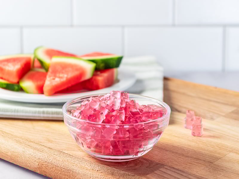 Homemade electrolyte gummies made with Paleovalley Watermelon Electrolytes, shaped like tiny bears and served in a glass bowl, with fresh watermelon slices in the background.