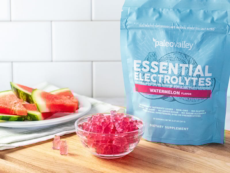 Homemade electrolyte gummies made with Paleovalley Watermelon Essential Electrolytes, served in a clear glass bowl beside the product pouch, with fresh watermelon slices in the background.